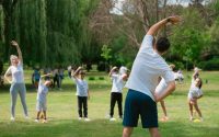 Children and instructors stretching in a park during a summer physical education class.
